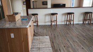 A spacious kitchen with wooden flooring, a marble countertop, and wooden stools.