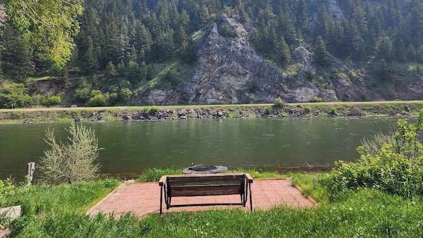 A bench overlooking a calm river with a forested mountain in the background.
