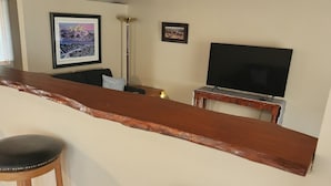 A bar area with wooden stools, a flat-screen TV, and framed pictures on the wall.