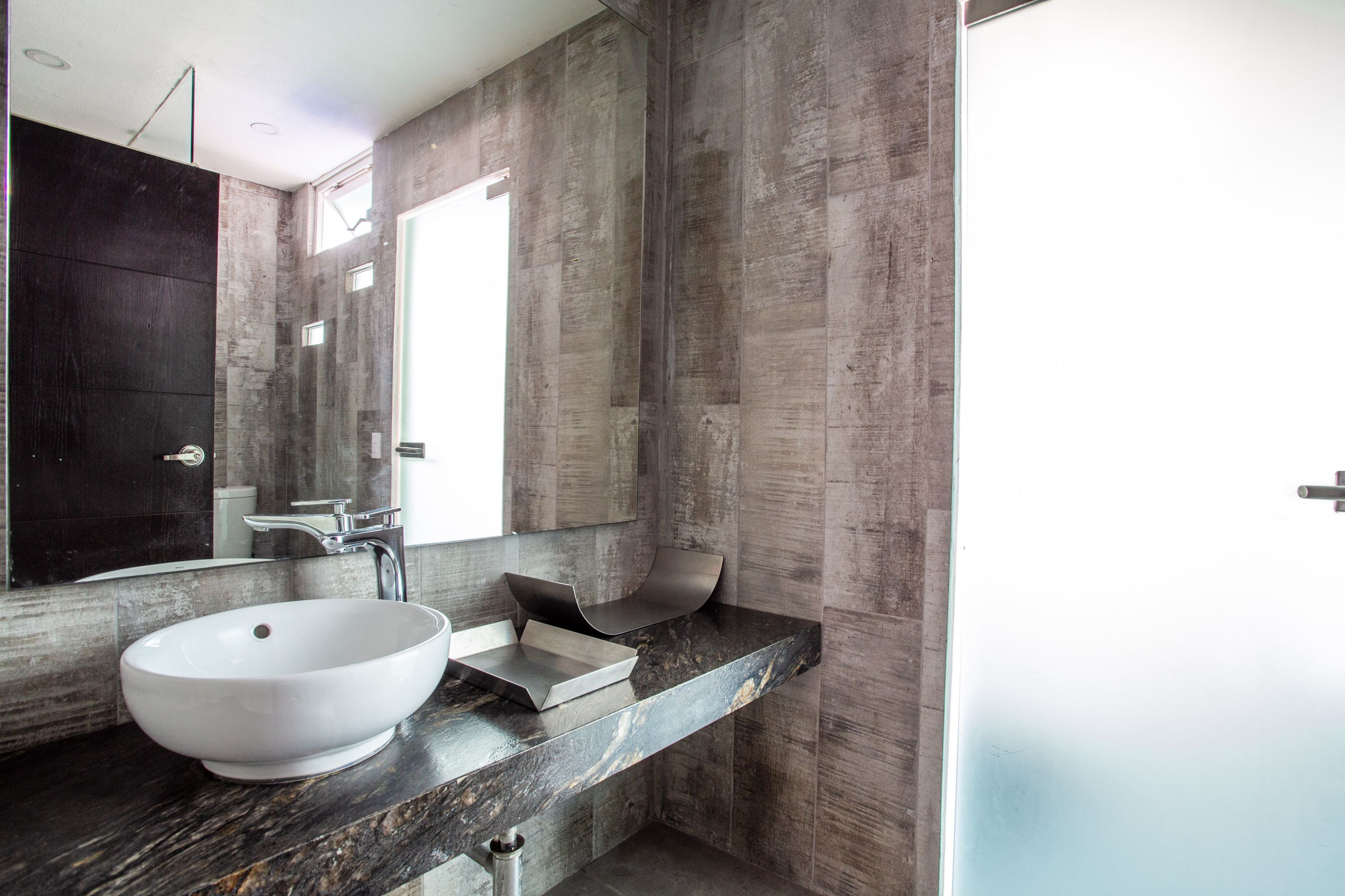 A modern bathroom with a large white vessel sink, a sleek black countertop, and a large mirror.