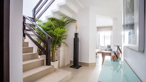 A modern interior with a staircase, a potted plant, a tall black column, and a glass coffee table. - Private Pool, Near Beach, Restaurants - Sleeps 11 (Puerto Vallarta)