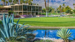 A modern building with large windows, a well-maintained lawn, and a pool area with agave plants. - Lakeside Luxe: Seven Lakes Golf & Country Club stylish condo (Palm Springs)