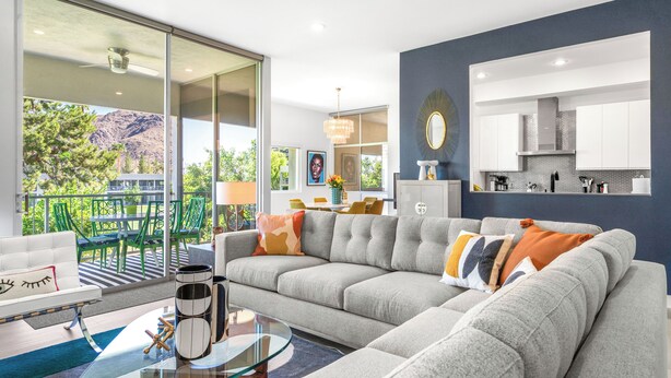 A modern living room with a sectional sofa, a glass coffee table, and a view of a balcony with outdoor furniture. - Lakeside Luxe: Seven Lakes Golf & Country Club stylish condo (Palm Springs)
