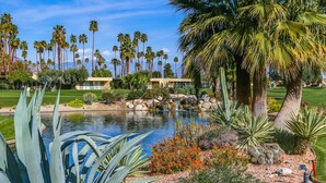 A landscaped garden with a pond, palm trees, and cacti. - Lakeside Luxe: Seven Lakes Golf & Country Club stylish condo (Palm Springs)
