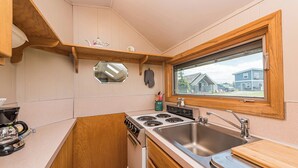 A compact kitchen with wooden cabinets, a stove, a sink, and a window with a view of houses. - Twin View Cottage - King, Futon, jetted tub (Sequim)