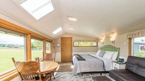 A bedroom with a bed, a sofa, a dining table with chairs, and large windows offering a view of the outdoors. - Twin View Cottage - King, Futon, jetted tub (Sequim)