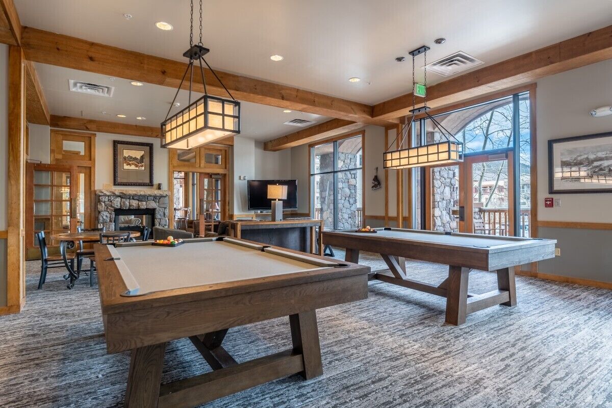 A pool table in a room with wooden beams, a fireplace, and large windows.