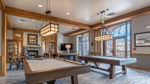 Une table de billard dans une pièce dotée de poutres en bois, d’une cheminée et de grandes fenêtres.