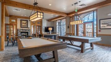 A pool table in a room with wooden beams, a fireplace, and large windows.