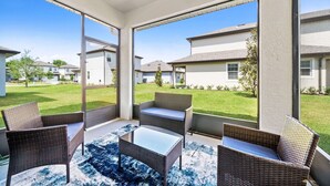 Un vaste patio aménagé avec des meubles en osier et une table en verre, offrant une vue sur une pelouse bien entretenue et les maisons voisines.