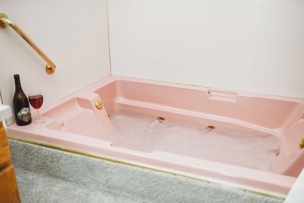 A pink bathtub with a bottle of wine and a glass on the side. - Fireplace Room - Water view, Jetted tub, King, Kitchen (Sequim)
