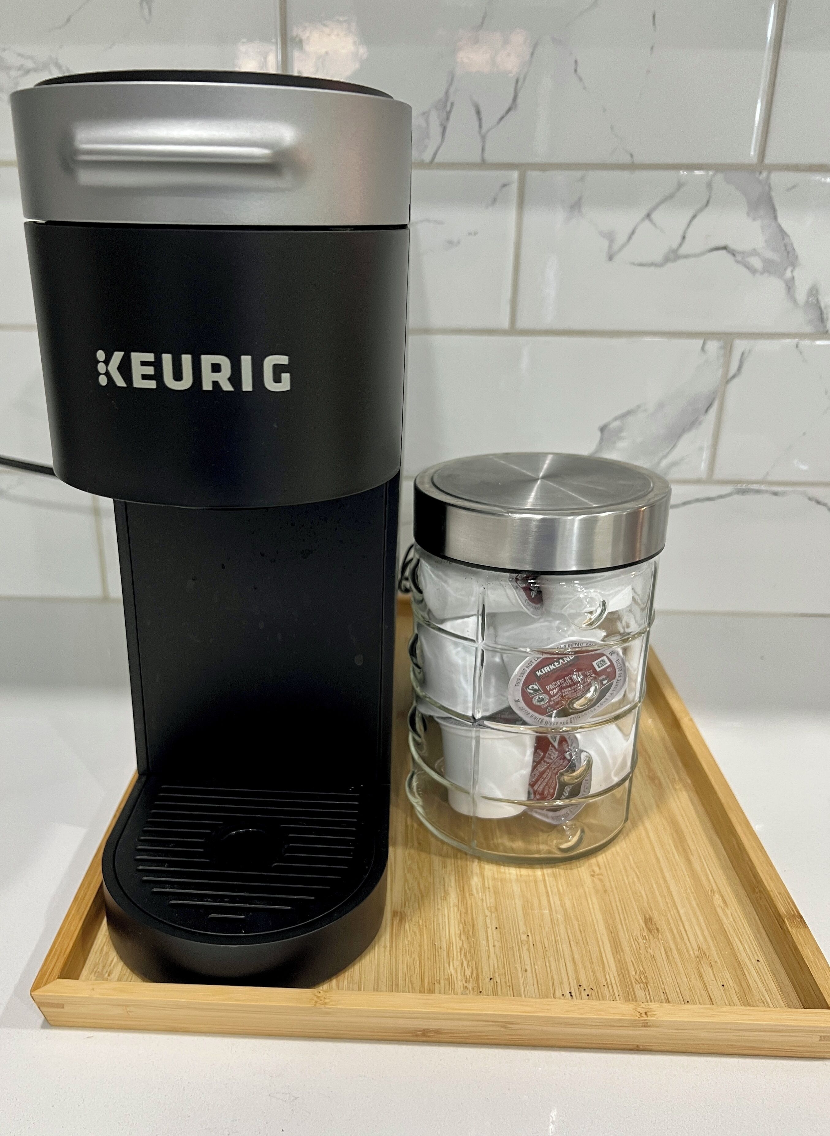 A Keurig coffee maker and a glass carafe with a lid on a wooden tray.