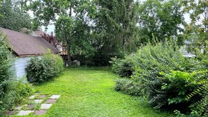 Un patio trasero bien cuidado, con césped, una terraza de madera y diversos arbustos y árboles.