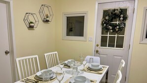 Comedor con una mesa blanca dispuesta para cuatro personas, rodeada de sillas blancas.