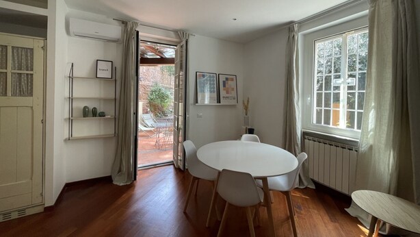 A room with a round table, chairs, a radiator, a window with curtains, and a door leading outside. - La Dolce VIta - The Secret Terrace (Roma)