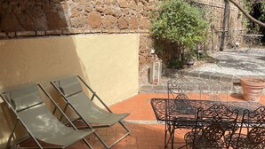 A patio area with lounge chairs and a metal table, adjacent to a stone wall and a potted plant. - La Dolce VIta - The Secret Terrace (Roma)