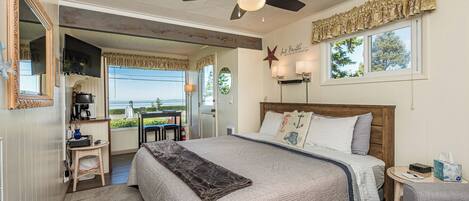 A bedroom with a bed, a ceiling fan, a window with curtains, a nightstand, and a view of the outdoors.