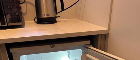 A refrigerator with a clear interior, a kettle on top, and a control panel.