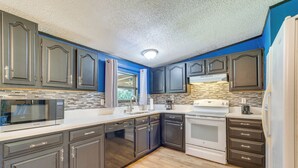 A modern kitchen with dark cabinetry, a microwave, dishwasher, and a stove. - Pet-Friendly Ocala Vacation Rental w/ Patio! (Ocala)
