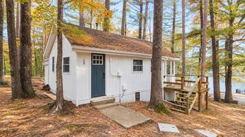 Une petite cabane avec une porte bleu foncé, une terrasse en bois et un chemin de pierres menant à l’entrée.