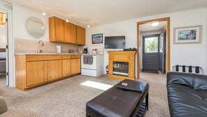 A compact living space with a kitchenette, a fireplace, a black leather bench, and a television. - Lavender Suite - King, full kitchen, jetted tub (Sequim)