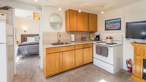 A compact kitchen with wooden cabinets, a white stove, a sink, and a television. - Lavender Suite - King, full kitchen, jetted tub (Sequim)