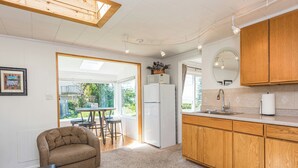 A modern kitchen with wooden cabinets, a refrigerator, and a dining area with a table and chairs. - Lavender Suite - King, full kitchen, jetted tub (Sequim)
