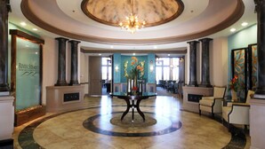 Un hall d’entrée avec une table ronde centrale, des colonnes et un lustre.