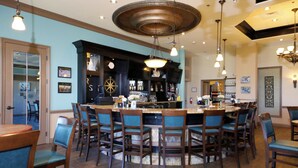 Un espace bar avec une table ronde entourée de chaises, un comptoir de bar avec des bouteilles et un ventilateur de plafond.