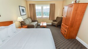 Ein Hotelzimmer mit einem großen Bett, einem Schlafsofa, einem Sessel, einem kleinen Tisch und einem Kleiderschrank.