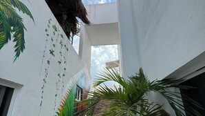 Una escalera estrecha con barandilla de piedra que lleva a un edificio blanco con un mural de palmeras y techo de paja.