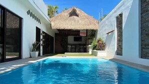 Una piscina con una estructura de techo de paja al fondo.