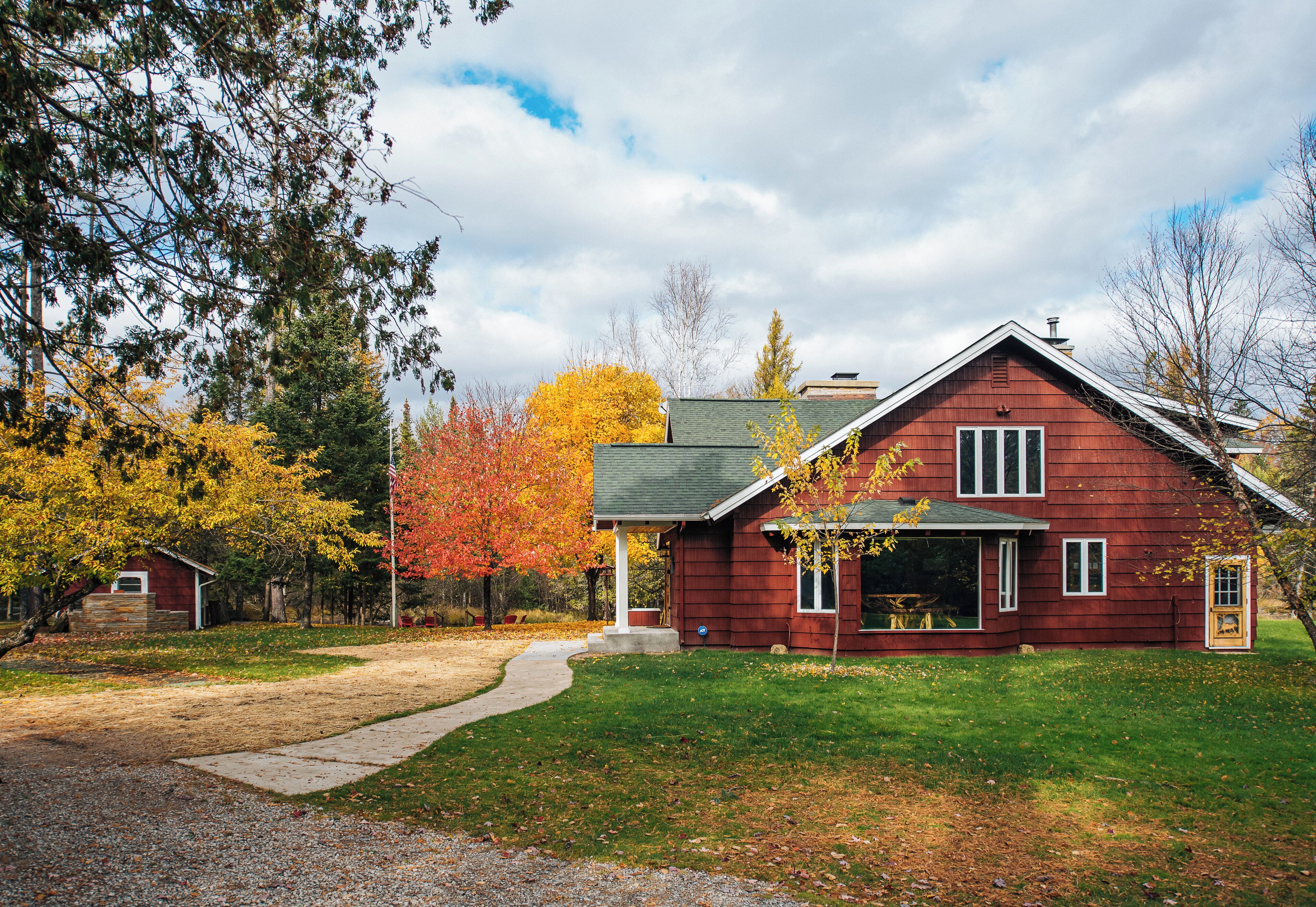 A red wooden house with a green lawn and a gravel driveway.