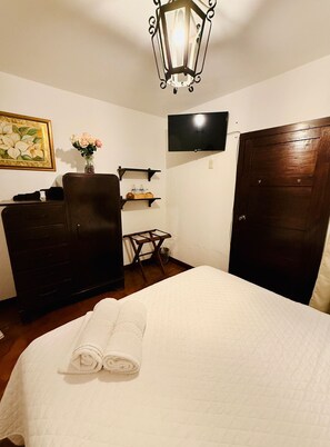 A hotel room with a bed, a dresser, a television mounted on the wall, and a wooden door. - Parador de Antigua (Antigua Guatemala)