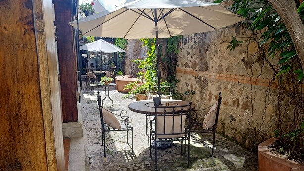 An outdoor patio area with a round table and chairs, a large umbrella, and potted plants. - Parador de Antigua (Antigua Guatemala)