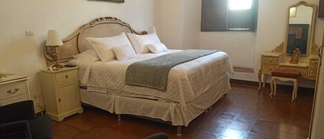 A bedroom with a bed, bedside table, lamp, dresser, chair, and a mirror.