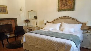 A neatly arranged bedroom with a large bed, bedside tables, a dresser, a mirror, and a fireplace. - Parador de Antigua (Antigua Guatemala)