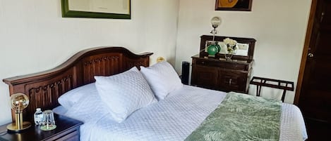 A neatly made bed with a quilted white duvet and pillows, a wooden nightstand with a lamp, and a dresser with a mirror and decorative items.