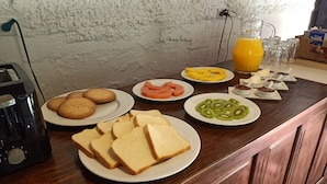A breakfast table with plates of toast, cookies, sliced watermelon, kiwi, and a pitcher of orange juice. - Parador de Antigua (Antigua Guatemala)