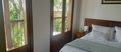 Un dormitorio con cama, mesita de noche y ventana con vistas a la vegetación.