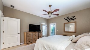 A bedroom with a bed, a ceiling fan, a dresser, a television, and a mirror. - Peaceful beachside rental (New Smyrna Beach)