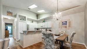 A modern kitchen with white cabinets, a central island, and a dining area with patterned chairs. - Peaceful beachside rental (New Smyrna Beach)