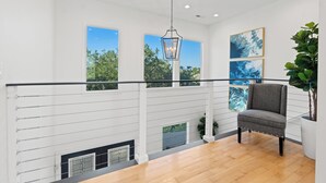 A spacious balcony with a view of trees, a grey chair, and artwork on the wall. - Marsh front home 10 min to beach and downtown- pet friendly! (Charleston)