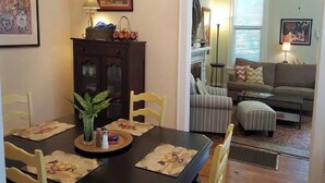 Un coin repas avec une table en bois, des chaises et un vase de fleurs. On y trouve également un meuble avec des portes en verre et une lampe fixée au mur.