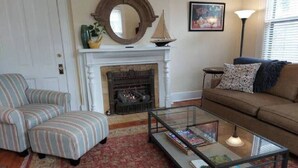 Un salon avec des fauteuils à rayures, une table basse en verre, une cheminée et un canapé.