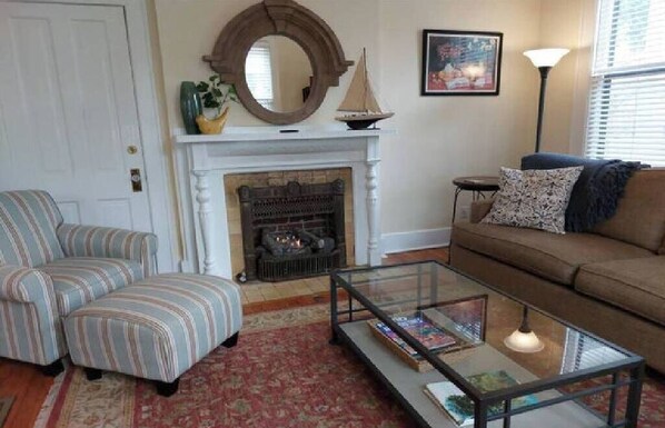 A living room with striped armchairs, a glass coffee table, a fireplace, and a sofa. - Barkley Cottage - 2 Bedroom (Little Rock)