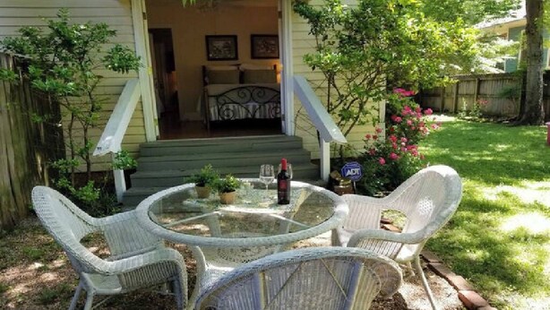 Eine Terrasse mit Korbstühlen und einem Glastisch, eine Treppe, die zu einem Schlafzimmer führt, und ein kleiner Garten mit Zaun und Baum.