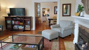 Ein Wohnzimmer mit Fernseher, Bücherregal, gestreiftem Sessel und Kamin.