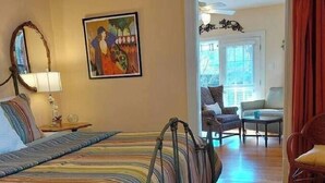 A hotel room with a bed, a chair, a table, and a painting on the wall.