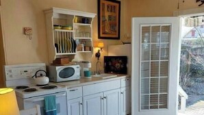 A compact kitchen with white cabinets, a stove, and a microwave. There's a dining table with a chair, and a glass door leading outside.
